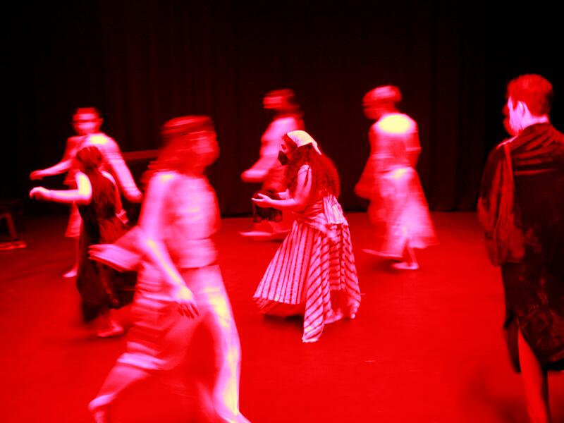 Raya Tuffaha is standing in the middle of a circle, wearing a striped skirt. The lighting is bright red